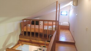 A loft bedroom with a wooden staircase, a small window, and a built-in bed. - Apartments Travarevic (Dubrovnik)