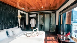 Una habitación de hotel con techo de madera, una cama con ropa de cama blanca, una toalla dispuesta en forma de corazón y una botella de vino sobre una mesa.