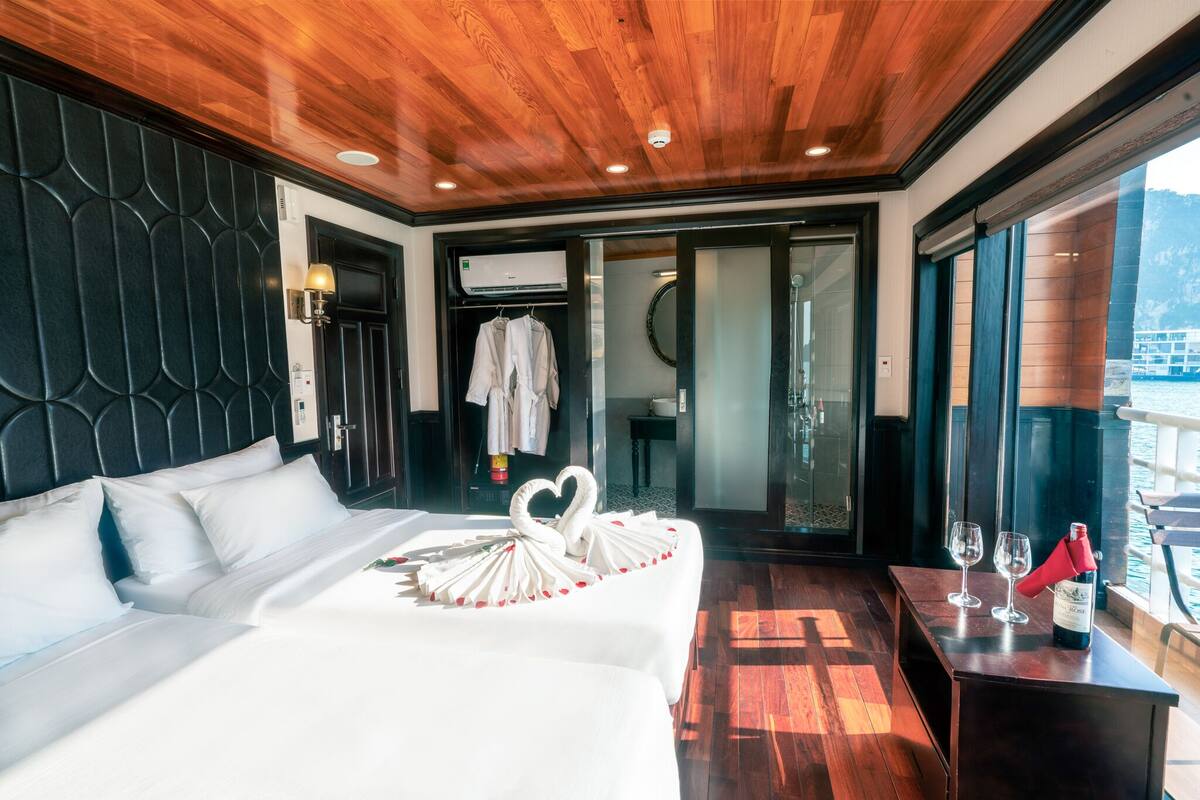 A hotel room with a wooden ceiling, a bed with white linens, a heart-shaped towel arrangement, and a bottle of wine on a table.