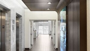 A modern hallway with a striped floor, elevators, and a glass wall on the right. - Residence Inn Richmond Midtown/Glenside (Richmond)