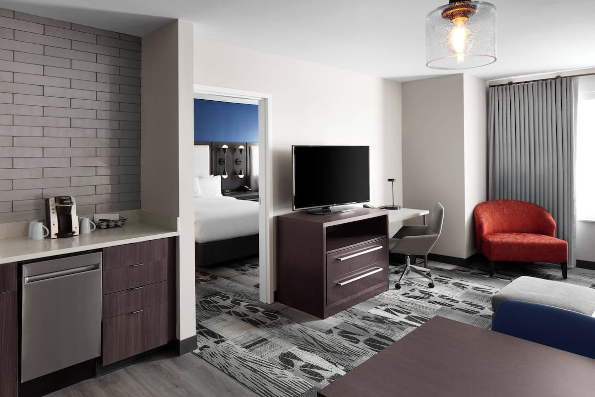 A modern hotel room with a flat-screen TV, a desk, a red chair, and a dining area.