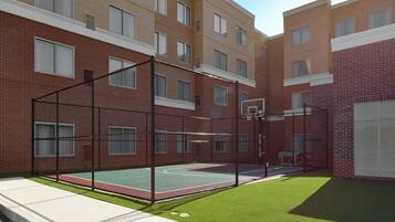 Una cancha de baloncesto con aro, rodeada por un edificio de ladrillo con varias ventanas.