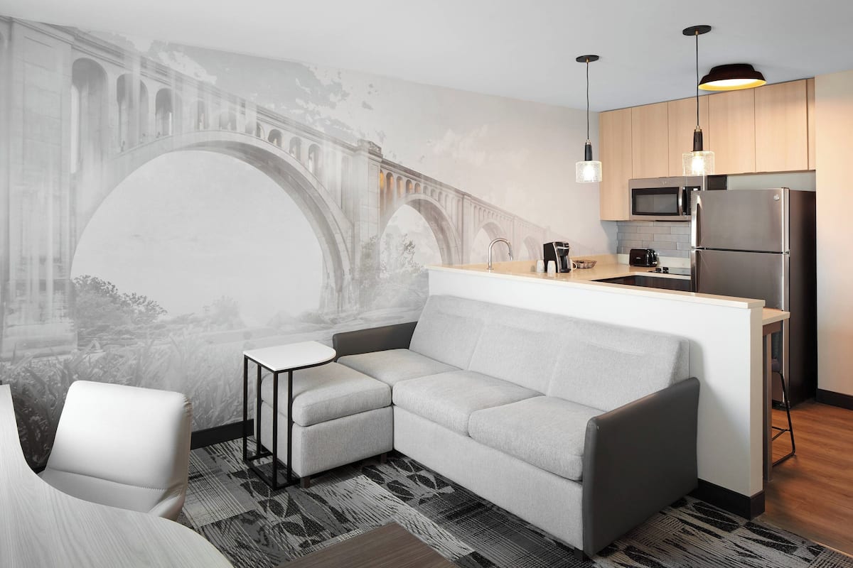A modern kitchen with a built-in microwave and refrigerator, a grey sofa, and a small table.