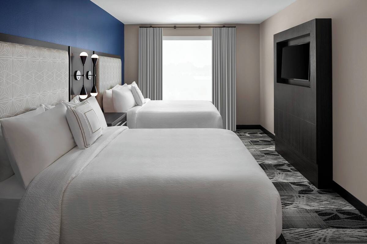A hotel room with two beds, a TV, and a large window with curtains.