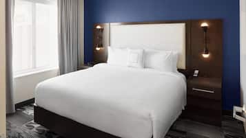 Ein Hotelzimmer mit einem großen Bett, einem Nachttisch mit Lampe, einem Fenster mit Vorhängen und einer blauen Wand.