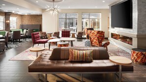 A modern lounge area with a brown leather sofa, patterned armchairs, and a flat-screen TV mounted on a brick wall. - Residence Inn Richmond Midtown/Glenside (Richmond)
