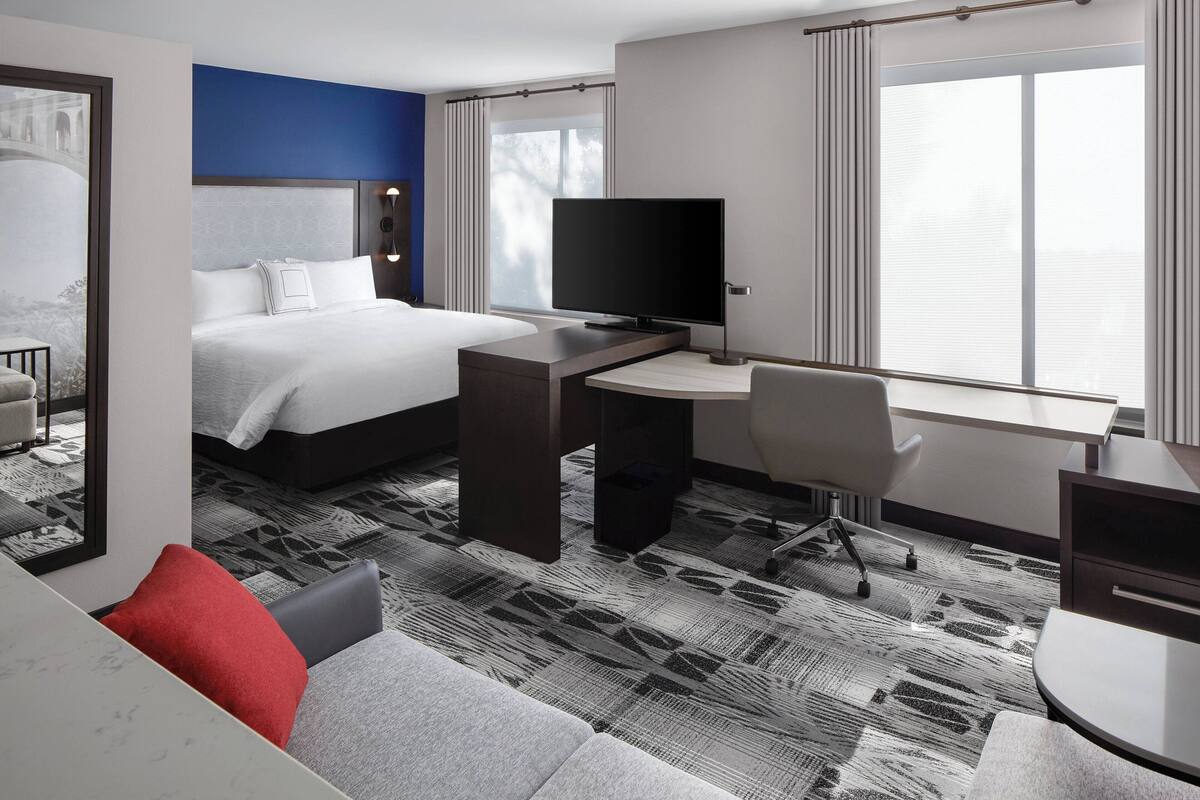 A hotel room with a bed, desk, TV, and a view of the outdoors.