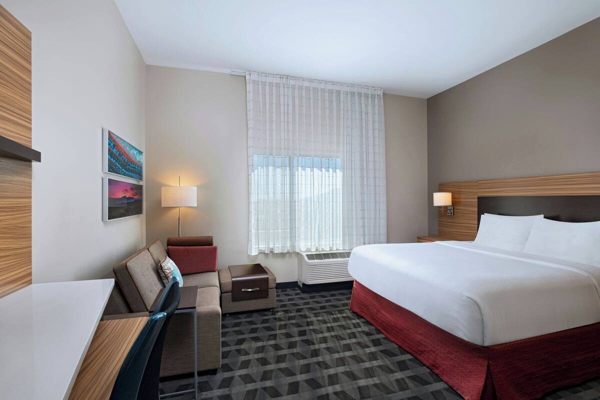 Une chambre d’hôtel équipée d’un lit, d’un bureau, d’une chaise, d’un canapé, d’une lampe et d’une fenêtre avec des rideaux.