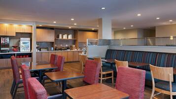 Un restaurante moderno con mobiliario de madera, una zona de estar con bancos acolchados y una cocina al fondo.