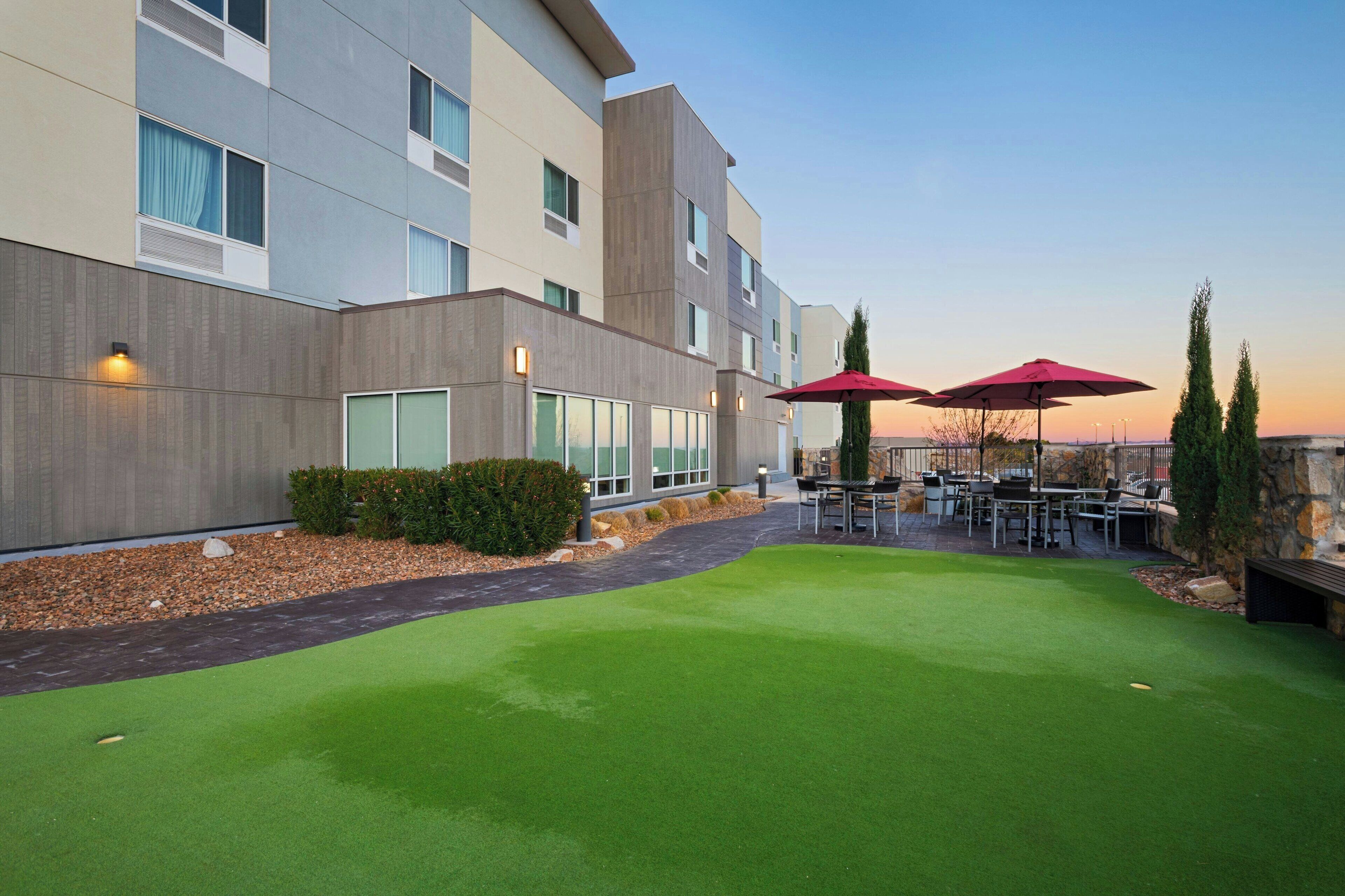 Un hôtel moderne doté d’une cour intérieure avec une pelouse artificielle, des sièges d’extérieur et une vue sur le coucher de soleil.