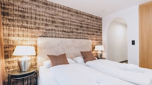 A hotel room with a large bed, two bedside tables with lamps, a textured wall, and an arched doorway. - Alpine City Living - TOP 11, City center & balcony (Zell am See)