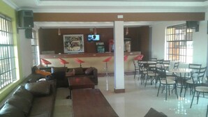 Eine Lobby mit einer Couch, Tischen und Stühlen. Es gibt eine Bar mit Hockern und einem Fernseher.
