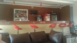 Eine Barbereich mit einer Theke, roten Barhocker und einem an der Wand montierten Fernseher.