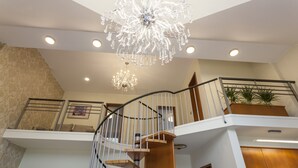 A multi-level interior with a wooden spiral staircase, a chandelier, and a plant on the upper level. - Duplex Penthouse Aparthotel Rosa (Podcetrtek)