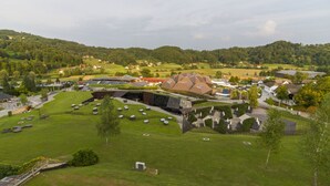 A modern building with a unique roof design, surrounded by a well-maintained lawn and a few trees. - Duplex Penthouse Aparthotel Rosa (Podcetrtek)