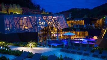 Um edifício moderno com fachada de vidro, área de estar externa e piscina.
