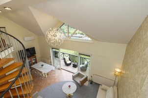 Amplia sala de estar con escalera, una mesa de comedor y un sofá. Incluye un balcón con mobiliario exterior y vistas al exterior.