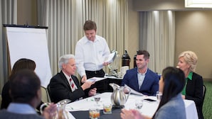 A business meeting with participants seated around a table with documents, a whiteboard, and a waiter serving. - Staybridge Suites Cedar Park - Austin N by IHG (Cedar Park)