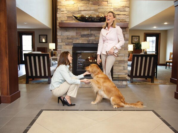 A lobby with a fireplace, seating area, and a dog interacting with a person. - Staybridge Suites Cedar Park - Austin N by IHG (Cedar Park)