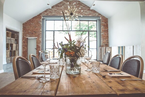 Una mesa de comedor dispuesta para seis personas, con un jarrón de flores, copas de vino y cubiertos.