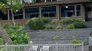 Ein modernes Gebäude mit großen Fenstern, einer Steinmauer und einem Kiesplatz mit Metallgeländer.