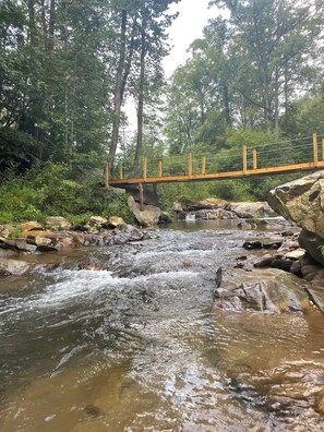 Eine Holzbrücke über einem plätschernden Bach, umgeben von Grün.