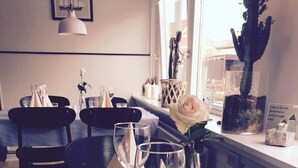 A dining area with a table set for two, a vase with a single white rose, and a window with a view of buildings. - Strandby Badehotel (Strandby)