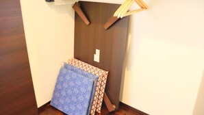 A corner of a room with a wooden door, a hanging rack with clothes, and folded blankets. - Vacation Rent Kanayama (Nagoya)