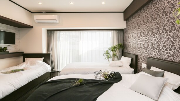 A modern hotel room with two beds, a large window with curtains, an air conditioning unit, and a patterned wall. - Vacation Rent Kanayama (Nagoya)