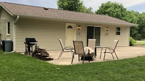 Ein Bungalow mit überdachter Terrasse, Grill und Gartenmöbeln.