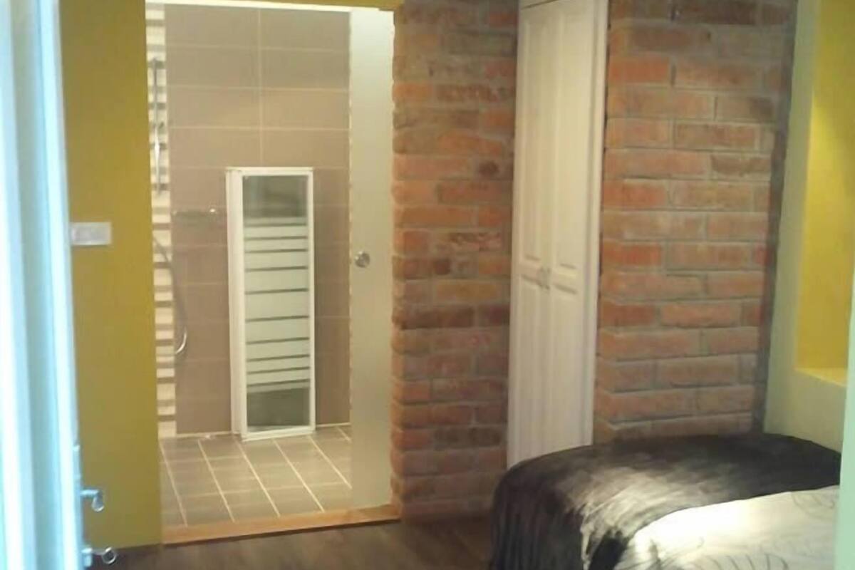 A bedroom with a bed, a brick wall, and a door leading to a bathroom.