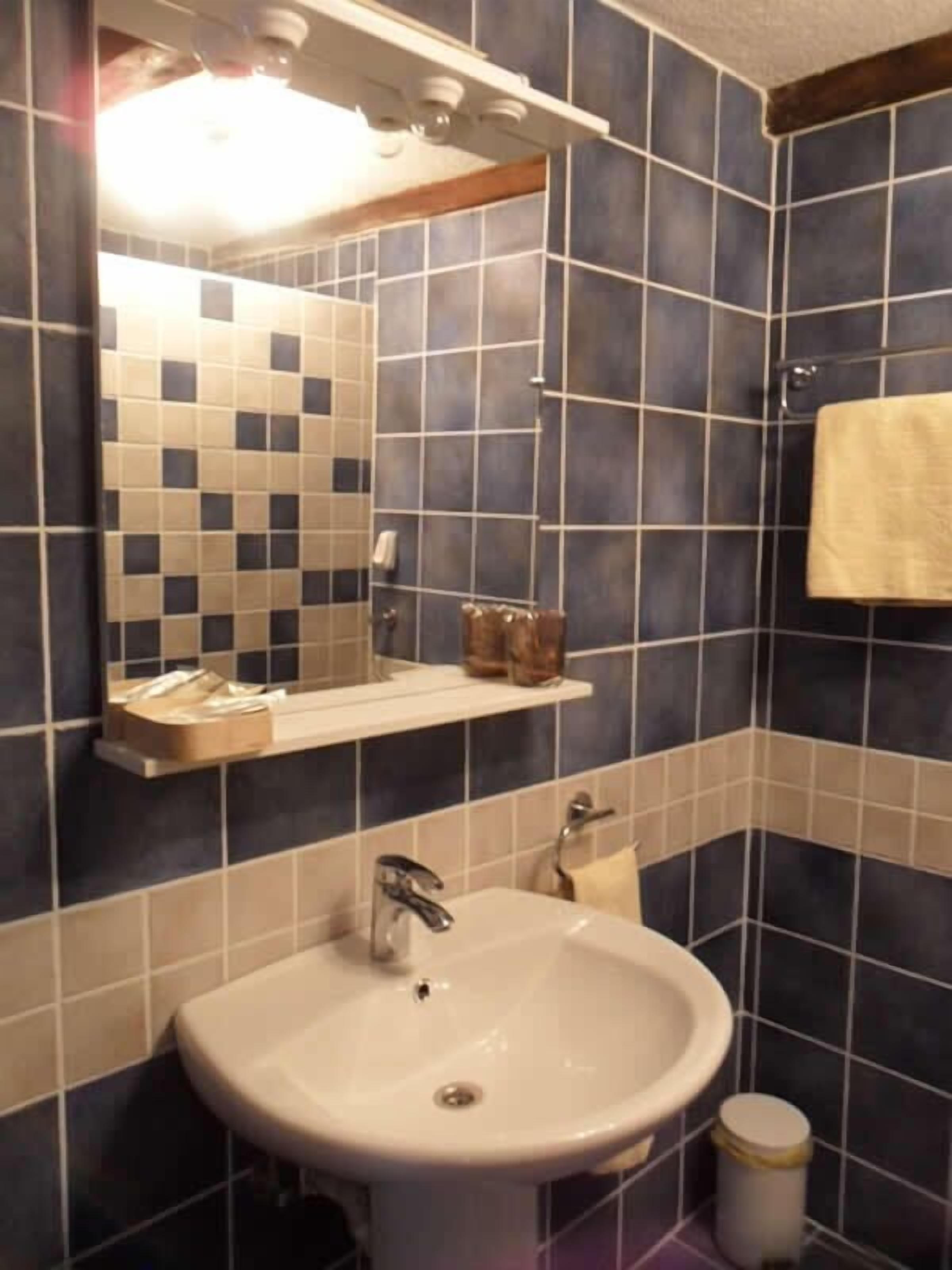 A bathroom with a white sink, a mirror, a towel hanging on the wall, and a shelf with toiletries.