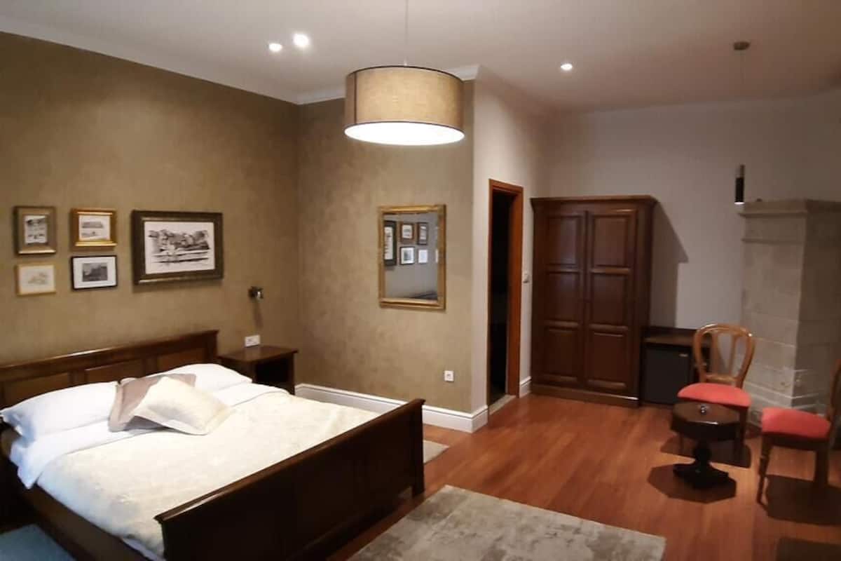 A bedroom with a wooden bed, a chair, a small table, and a mirror on the wall.
