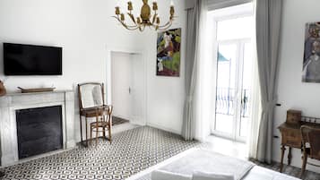 Quarto de hotel com lareira, cama com almofadas, uma cadeira, escrivaninha, televisão e um quadro na parede.