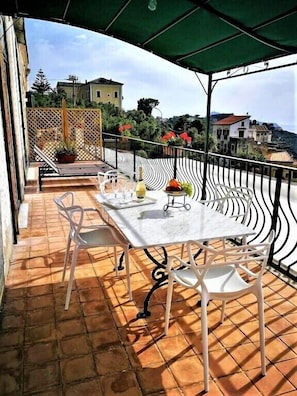 A terrace with a table and chairs, a potted plant, and a view of buildings in the background. - Artevilla Relais (Massa Lubrense)