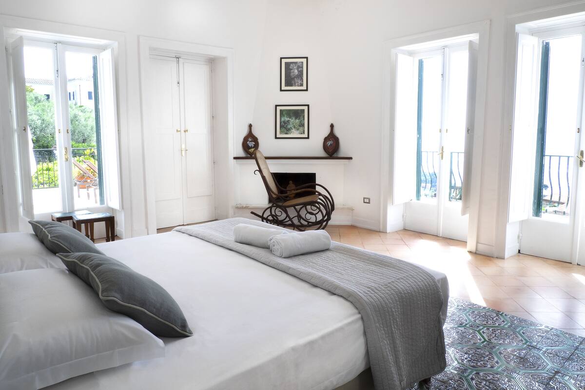 A bedroom with a large bed, a fireplace, and a balcony.