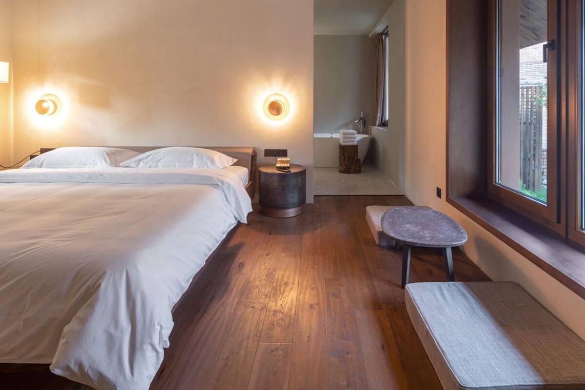 Une chambre avec deux lits, un coin salon, une fenêtre et une salle de bain visible à travers une porte ouverte.