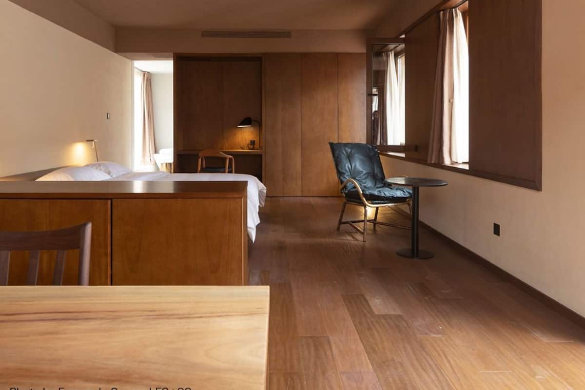 Une pièce spacieuse avec un plancher en bois, un coin repas comprenant une table et des chaises, une grande fenêtre avec des rideaux et un petit coin salon avec un fauteuil et une table.