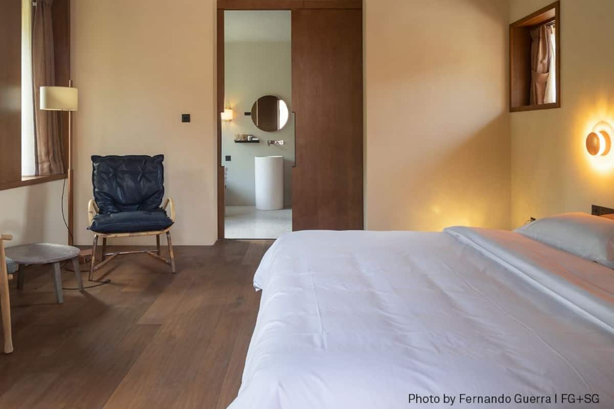 Une chambre d’hôtel avec un grand lit, une chaise, un bureau et une salle de bain visible à travers une porte ouverte.
