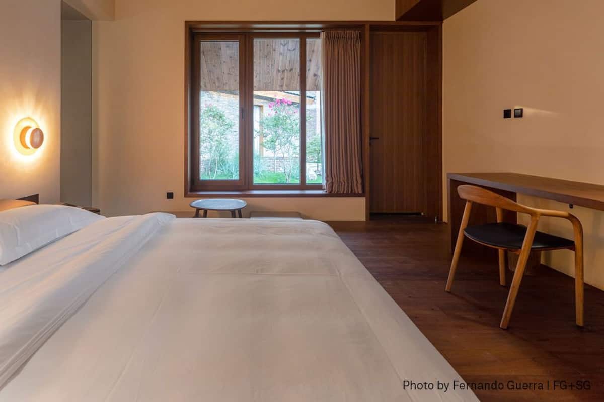 Une chambre moderne avec un grand lit, une petite table et une fenêtre avec des rideaux.