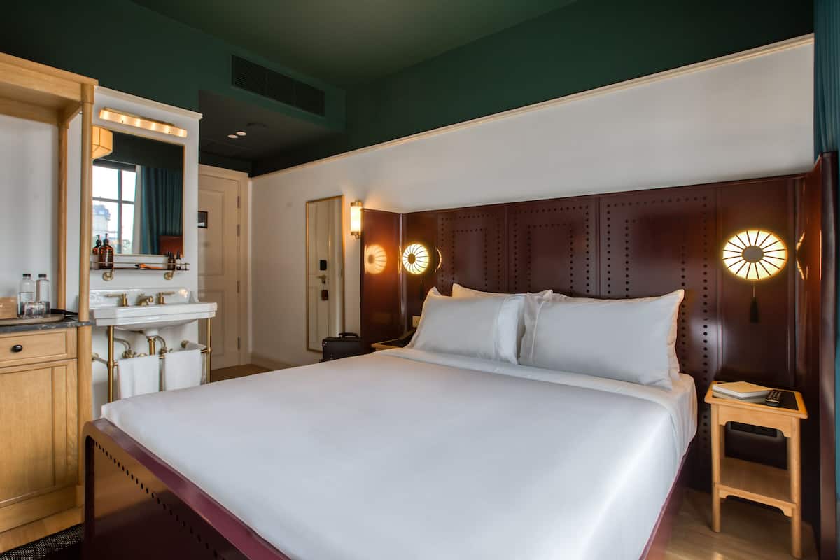 Une chambre d’hôtel avec un grand lit, une coiffeuse avec un miroir et une table de chevet avec une lampe.
