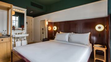 A hotel room with a large bed, a vanity with a mirror, and a nightstand with a lamp.