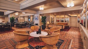 Een ruime hotellobby met hoge plafonds, meerdere eetgedeeltes en een centraal zitgedeelte met rieten meubels.