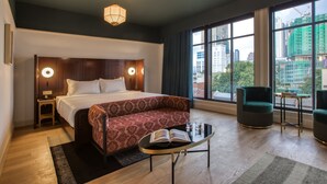 Een moderne hotelkamer met een groot bed, een bank, een klein tafeltje en een stadszicht door grote ramen.