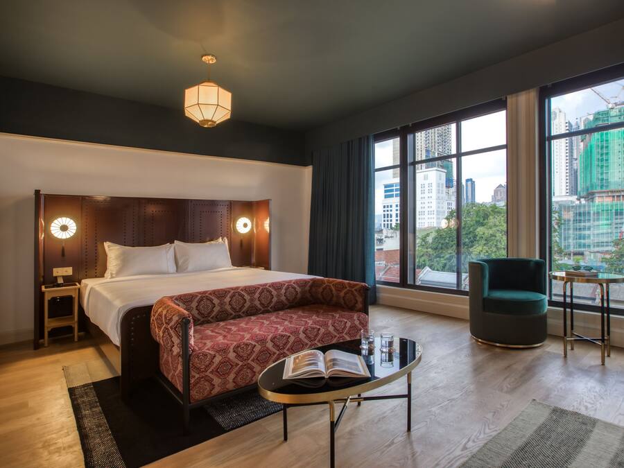 Habitación de hotel moderna con una cama grande, un sofá, una mesita y vistas a la ciudad a través de amplias ventanas.