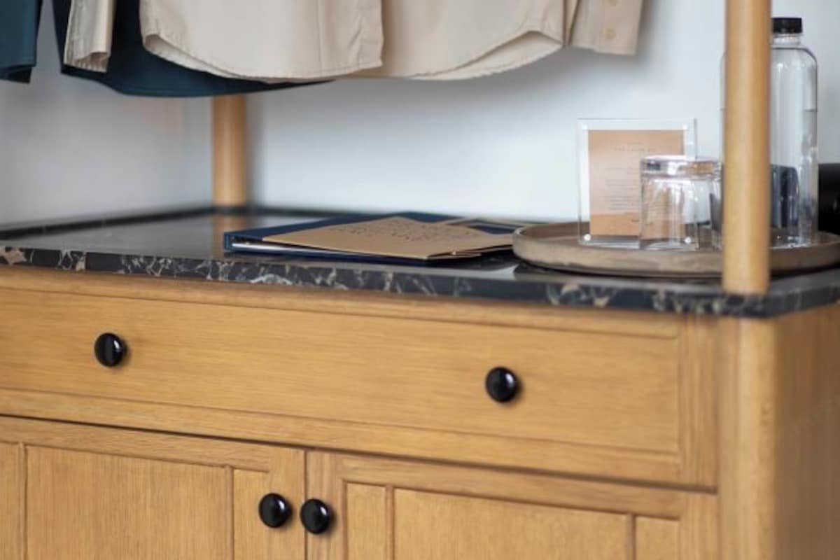 Un mueble de madera con pomos negros, un tarro de vidrio y un folleto sobre una encimera de mármol.