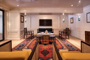 A room with a large flat-screen TV mounted on the wall, a table with two chairs, a decorative rug, and a sofa.