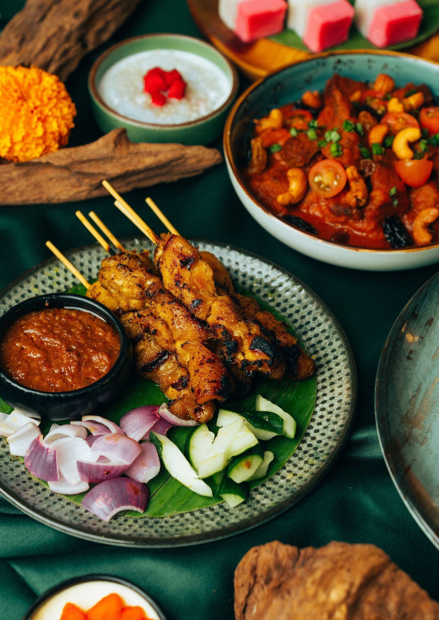 A variety of dishes including grilled meat skewers, a bowl of curry, and a plate of sliced vegetables.