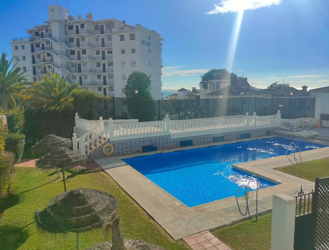 A swimming pool with a white fence, a white building in the background, and a clear sky.