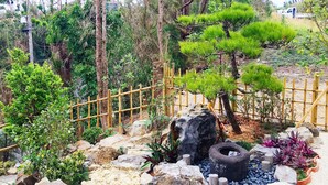 A landscaped garden with various plants, rocks, and a wooden fence. - Ocean Aroha Resort (Onna)